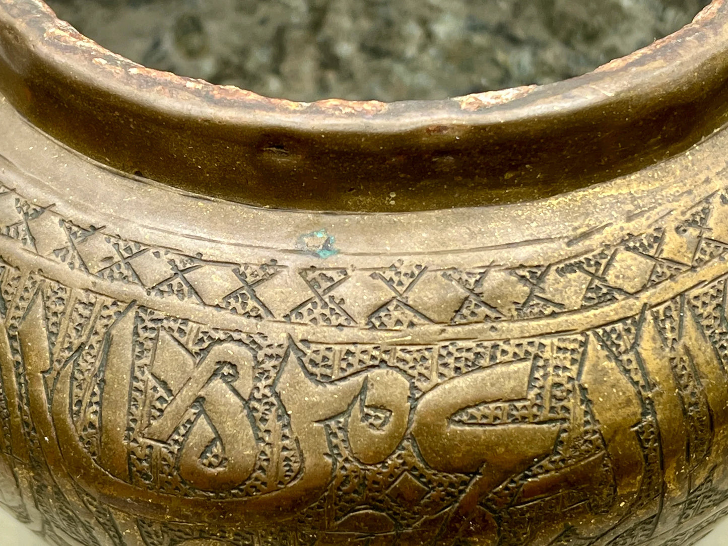 Close-up of a bronze pot with intricate designs and Arabic text.