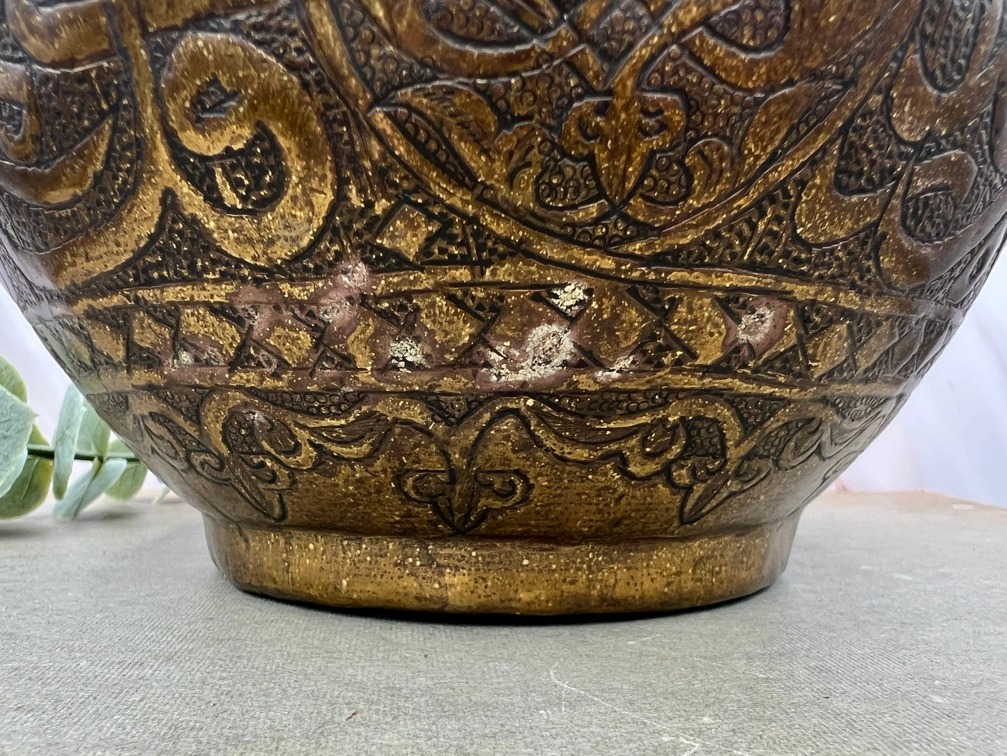 Close-up of a bronze vase with intricate patterns on a textured surface.