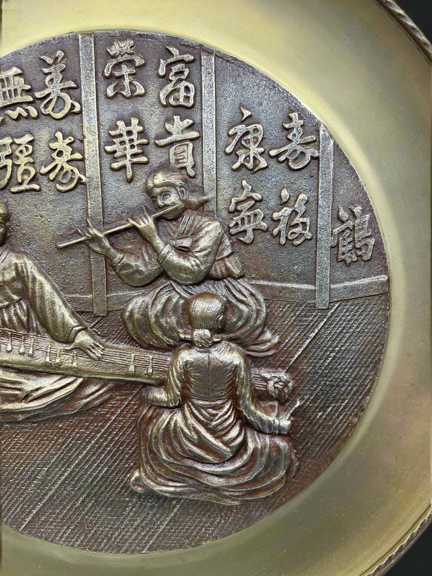 Bronze plaque with intricate design and text, featuring two figures and classical architecture.
