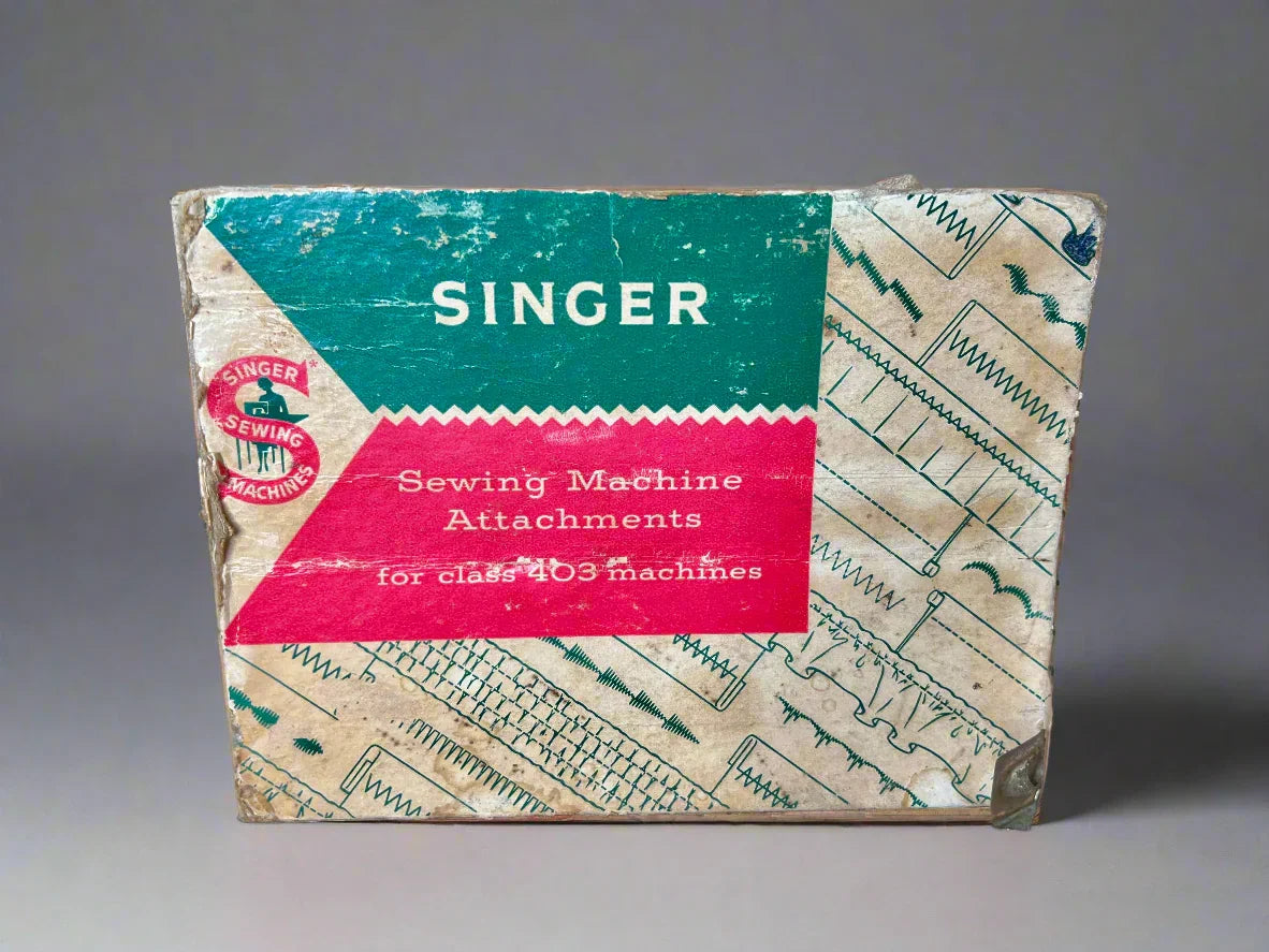 Vintage Singer sewing machine attachments box on a dark surface