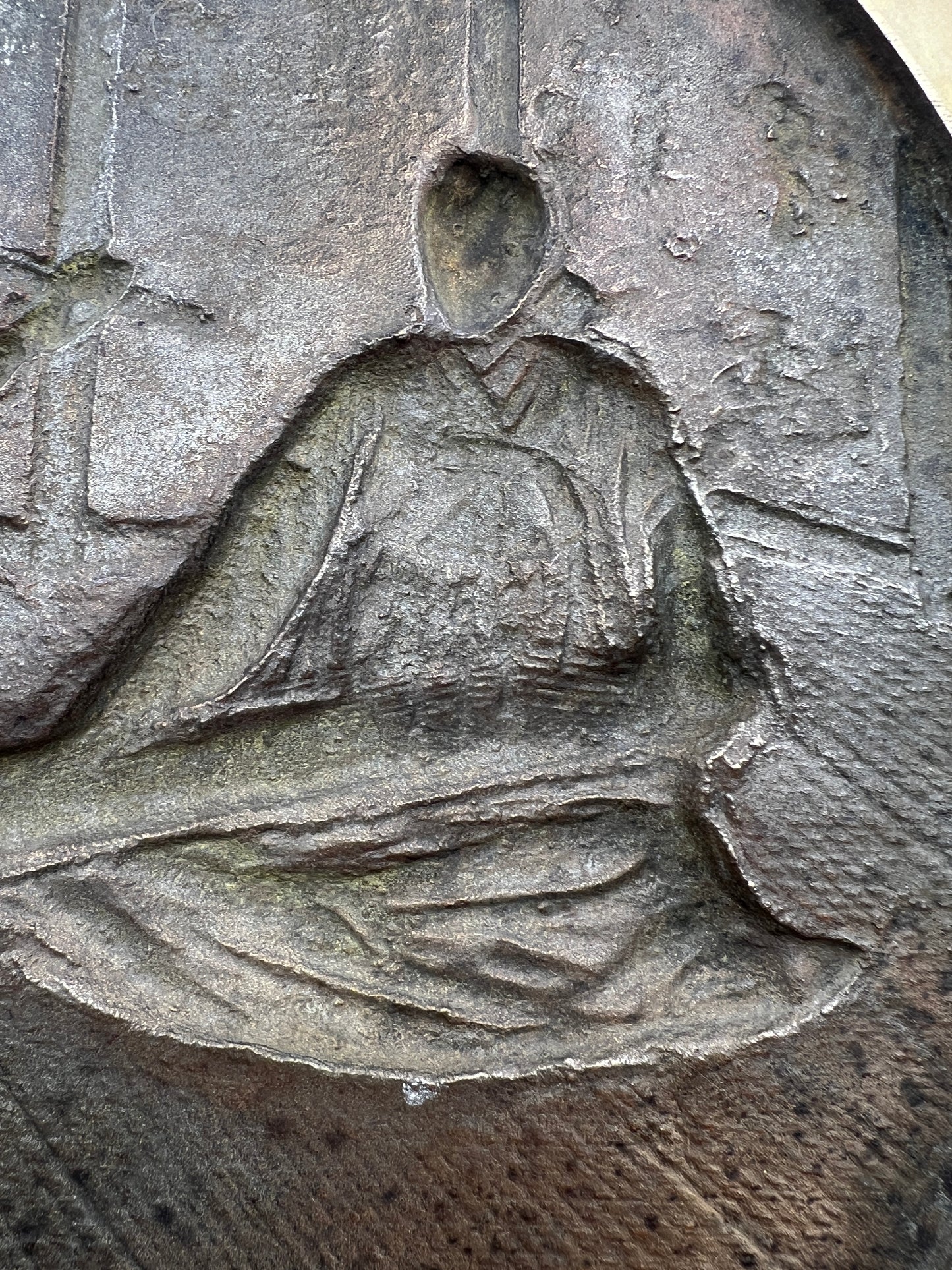 Stone carving of a person holding a book or scroll on a textured stone surface