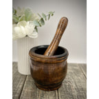 Antique wooden mortar and pestle with dark, worn patina; pestle resting inside.