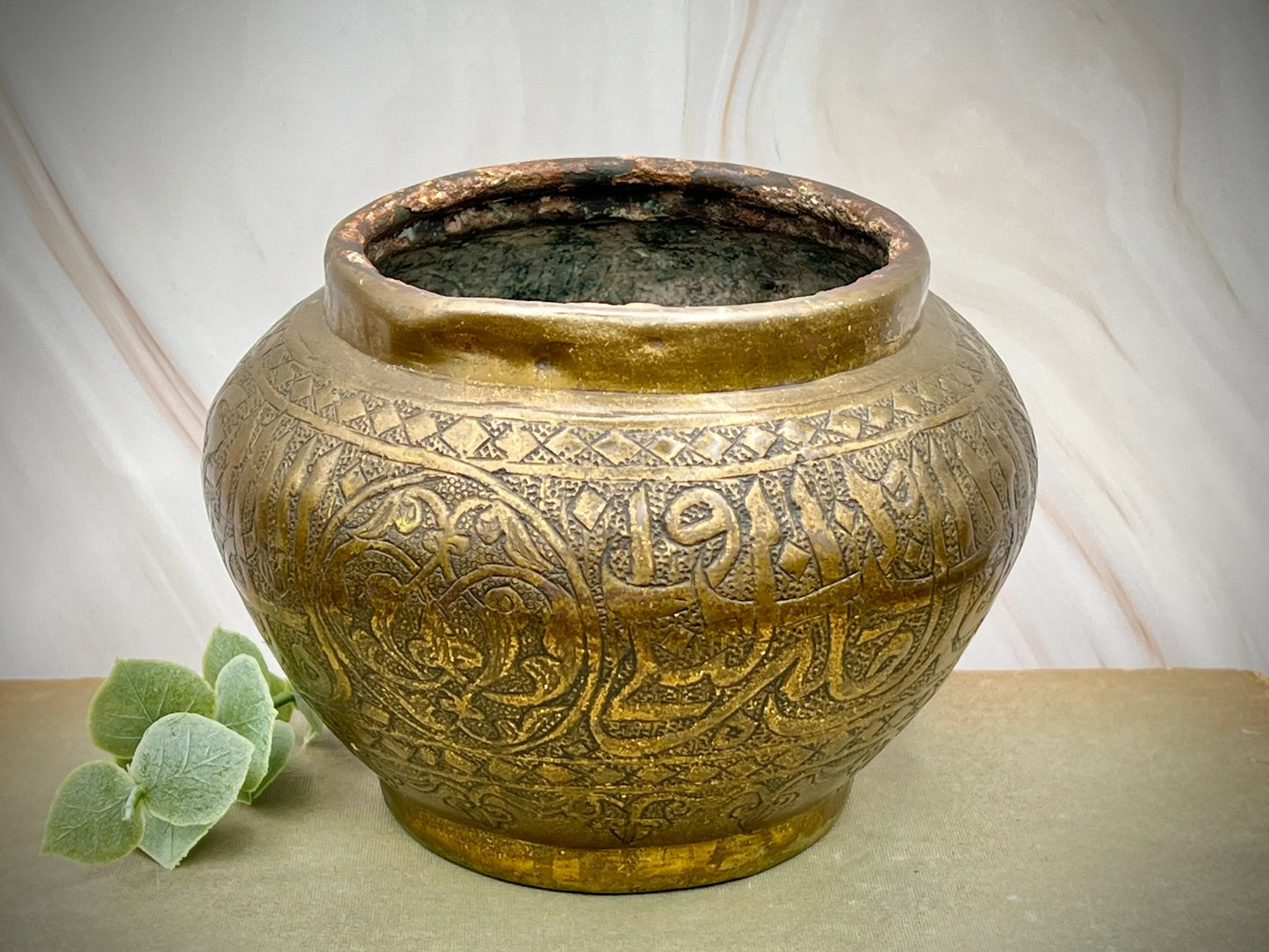 Decorative bronze pot with intricate designs on a neutral background