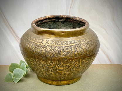 Decorative bronze pot with intricate designs on a neutral background