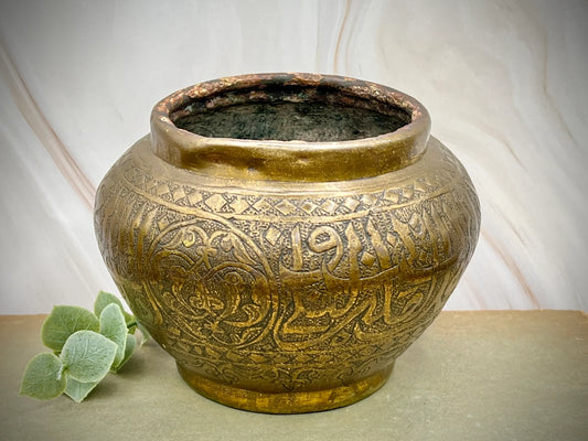 Decorative bronze pot with intricate designs on a neutral background