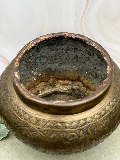 Close-up of a textured bronze pot with intricate designs on a light background