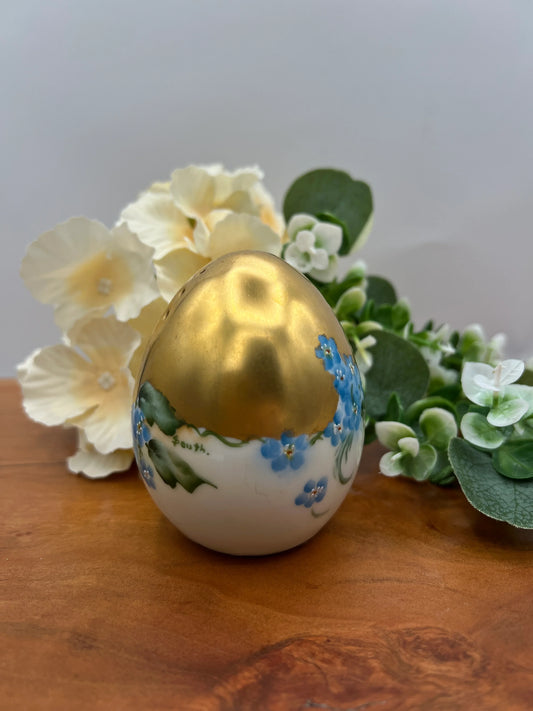Decorative egg with gold top and floral patterns on a wooden surface with flowers in the background