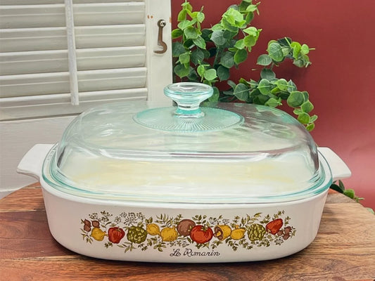 Vintage Pyrex dish with colorful fruit pattern on a wooden board against a red wall.