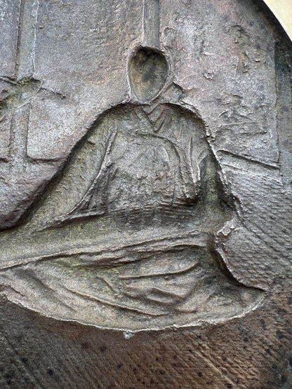 Stone carving of a person holding a book or scroll on a textured stone surface