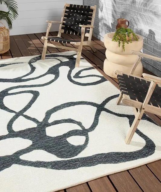 Outdoor setting with a patterned rug, wooden chairs, and potted plants on a wooden deck.