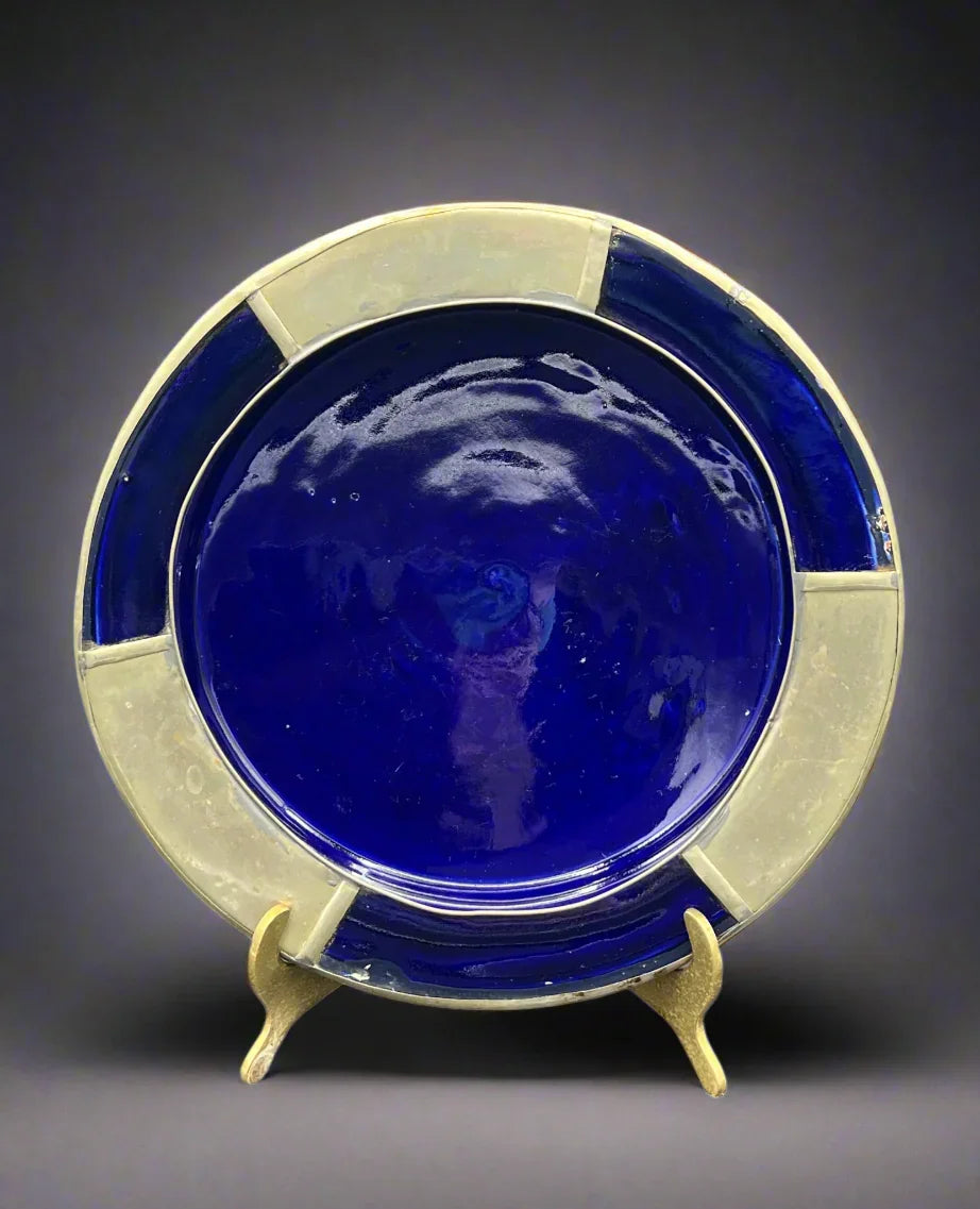 Ceramic plate with blue center and white rim on a stand against a dark background
